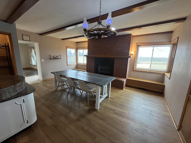 dining area with wood-type flooring, an inviting chandelier, a fireplace, and beam ceiling