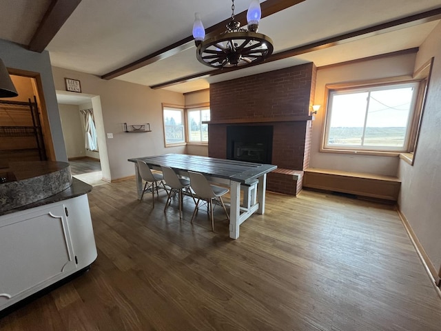 dining room featuring beamed ceiling, a brick fireplace, and hardwood / wood-style floors