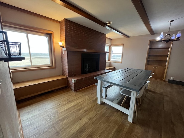 dining room featuring a fireplace, beam ceiling, wood-type flooring, and a chandelier