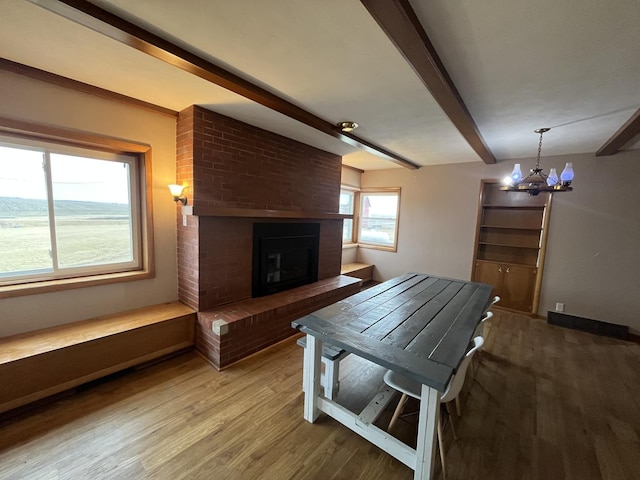 unfurnished dining area featuring an inviting chandelier, hardwood / wood-style floors, beam ceiling, and a fireplace