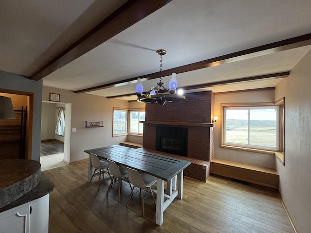 dining room featuring beamed ceiling, a chandelier, a brick fireplace, and hardwood / wood-style flooring