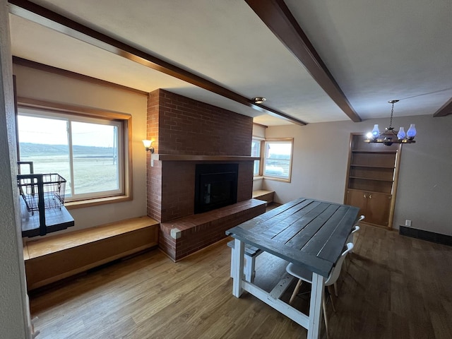 dining room with a water view, an inviting chandelier, wood-type flooring, a brick fireplace, and beam ceiling