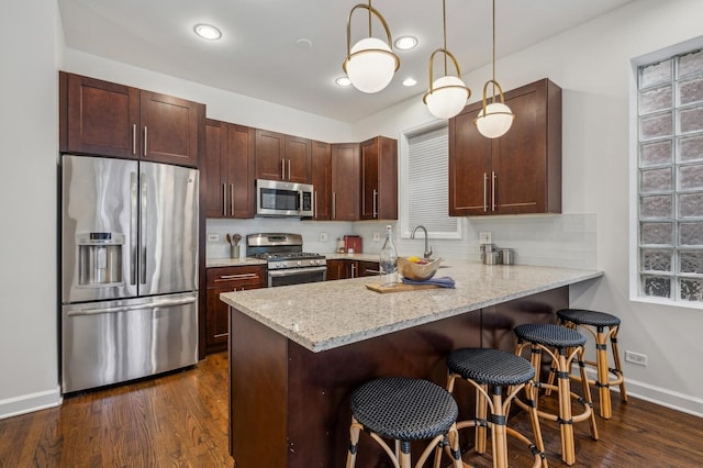 kitchen featuring pendant lighting, dark wood-type flooring, light stone countertops, and appliances with stainless steel finishes