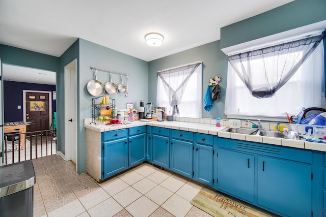 kitchen featuring blue cabinets, sink, tile counters, and light tile patterned floors