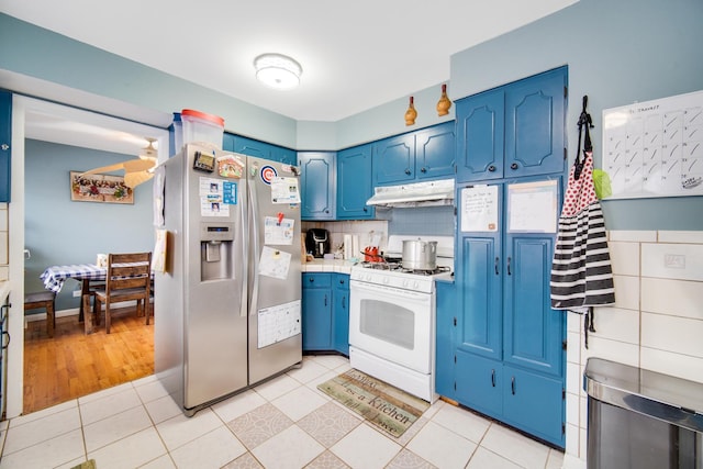 kitchen featuring light tile patterned floors, stainless steel fridge, blue cabinetry, tasteful backsplash, and white gas stove