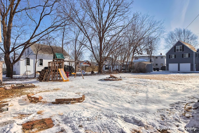 yard layered in snow featuring a playground and a garage