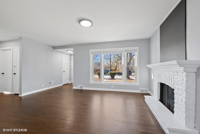 unfurnished living room with a brick fireplace and dark wood-type flooring