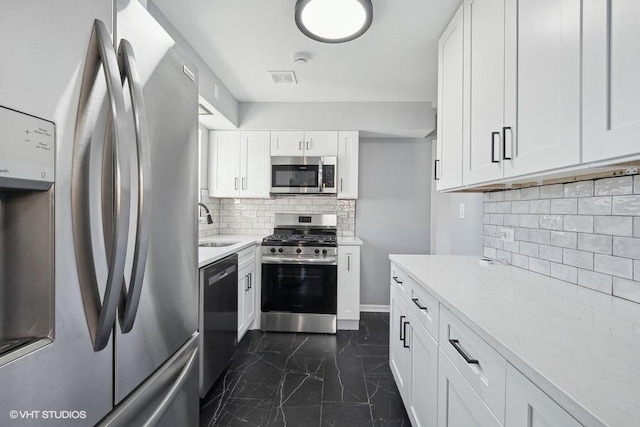 kitchen featuring sink, tasteful backsplash, white cabinetry, light stone countertops, and stainless steel appliances