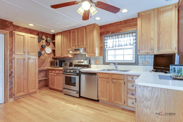 kitchen with sink, wooden walls, stainless steel appliances, decorative backsplash, and light wood-type flooring