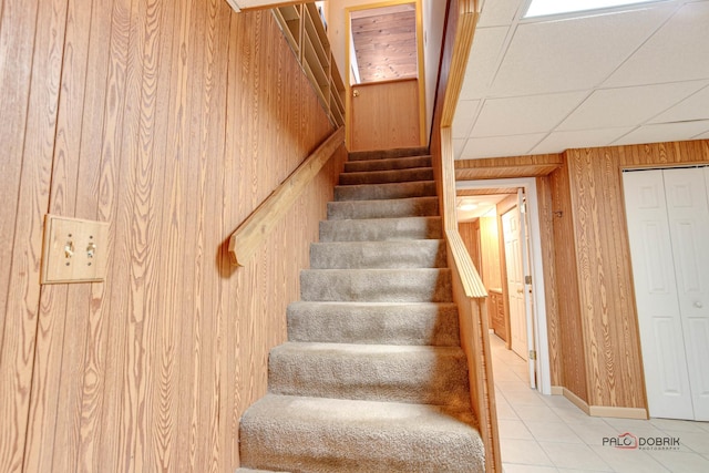 stairway featuring tile patterned floors, wooden walls, and a drop ceiling