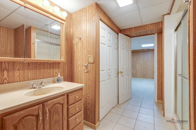 bathroom featuring walk in shower, tile patterned floors, vanity, wooden walls, and a drop ceiling