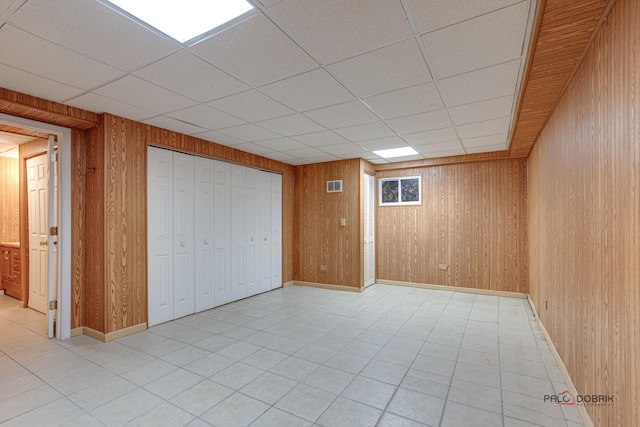 basement with a paneled ceiling and wood walls