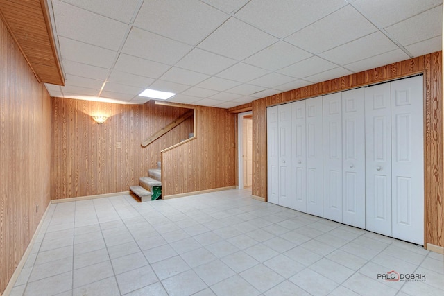 basement featuring light tile patterned flooring, a paneled ceiling, and wooden walls