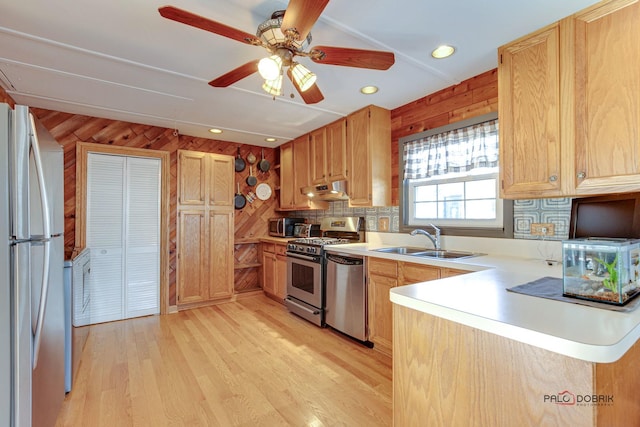 kitchen featuring sink, light hardwood / wood-style flooring, appliances with stainless steel finishes, kitchen peninsula, and wood walls