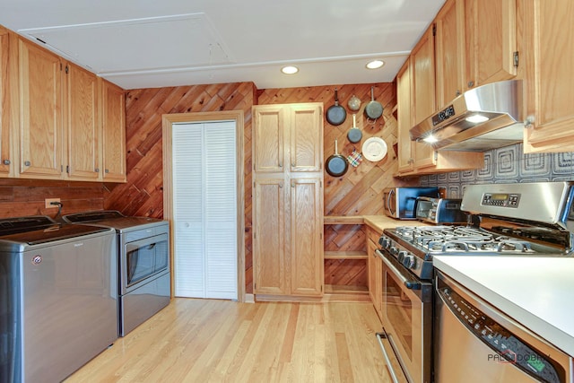 kitchen featuring light hardwood / wood-style flooring, appliances with stainless steel finishes, separate washer and dryer, exhaust hood, and wood walls