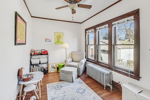 sitting room with hardwood / wood-style floors, radiator heating unit, ornamental molding, and ceiling fan