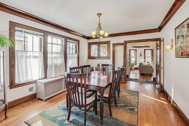 dining area with hardwood / wood-style floors, a notable chandelier, radiator heating unit, and ornamental molding