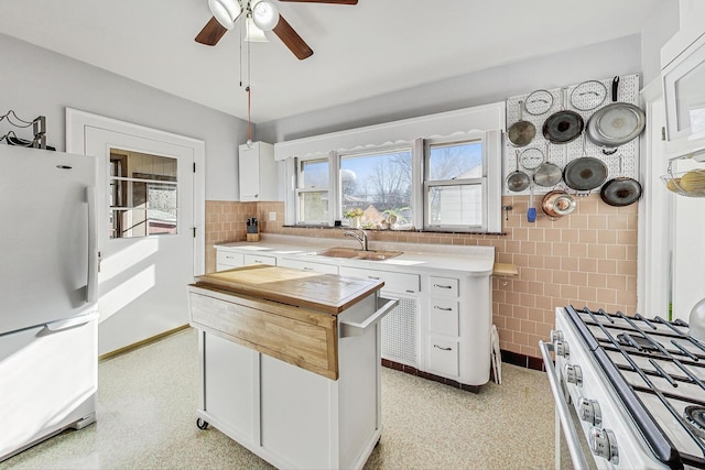 kitchen featuring sink, tile walls, fridge, stainless steel range, and white cabinets