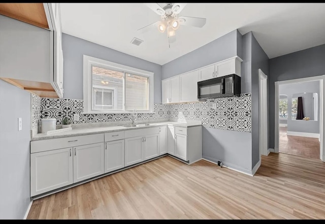 kitchen with white cabinets, light hardwood / wood-style floors, sink, backsplash, and ceiling fan