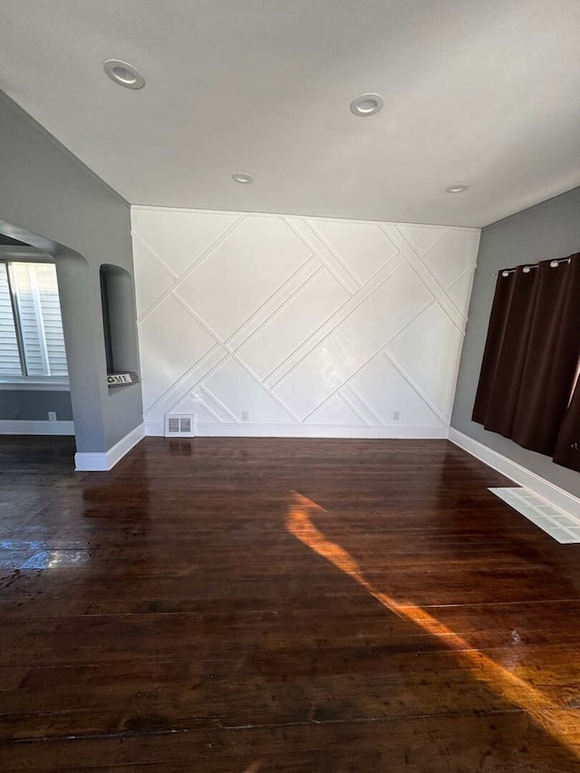 unfurnished room with baseboards, visible vents, a decorative wall, and wood finished floors