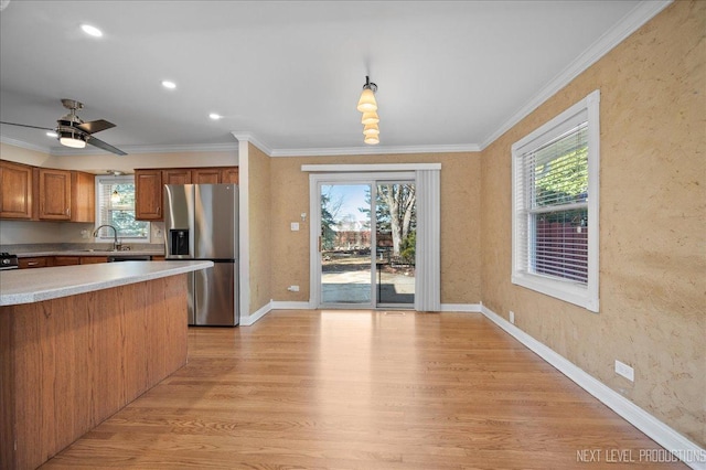 kitchen with crown molding, light wood-type flooring, a wealth of natural light, stainless steel refrigerator with ice dispenser, and a sink