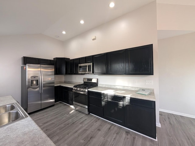 kitchen with high vaulted ceiling, sink, stainless steel appliances, and hardwood / wood-style flooring