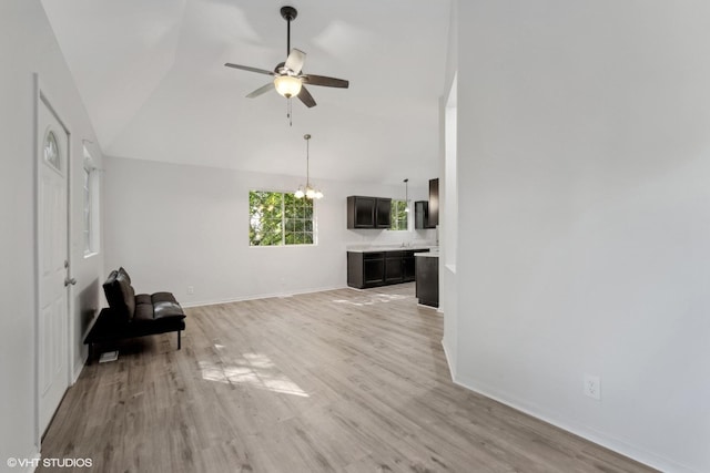 unfurnished living room featuring lofted ceiling, ceiling fan with notable chandelier, and light hardwood / wood-style flooring