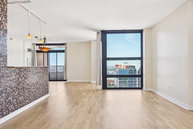 spare room with light hardwood / wood-style floors, a wall of windows, and track lighting