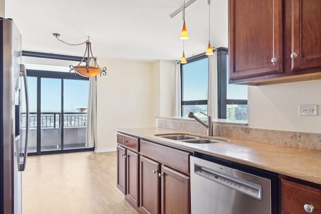 kitchen with appliances with stainless steel finishes, rail lighting, sink, decorative light fixtures, and light wood-type flooring