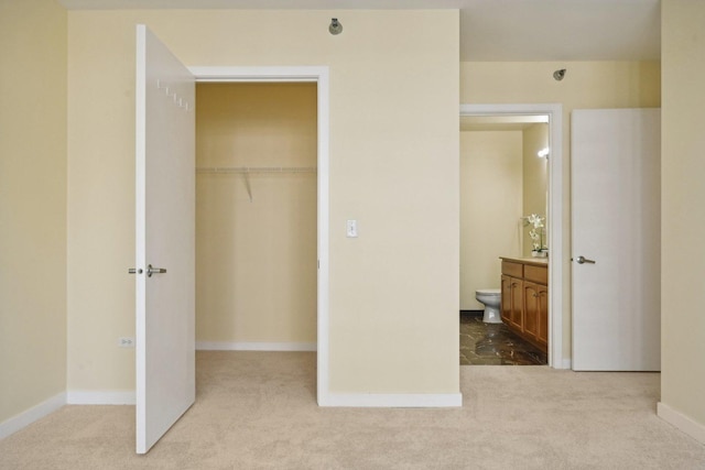 unfurnished bedroom with a closet, ensuite bathroom, a spacious closet, and light carpet