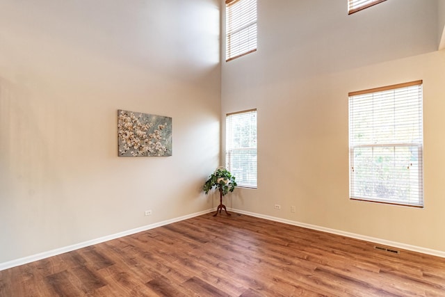 spare room featuring a towering ceiling, a wealth of natural light, and hardwood / wood-style floors