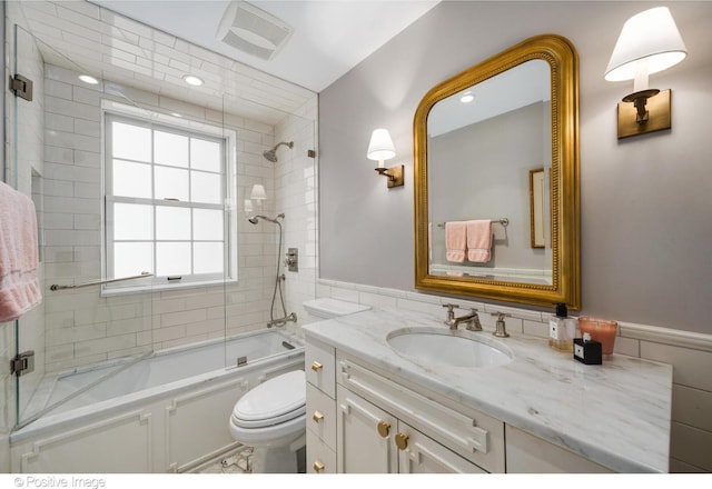 full bathroom with vanity, toilet, tiled shower / bath combo, and tile walls