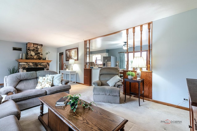 carpeted living room with a stone fireplace and ceiling fan