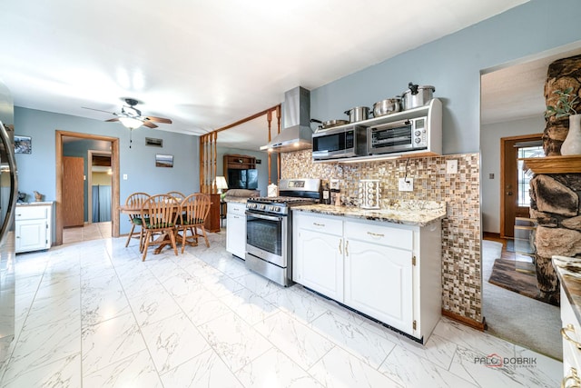 kitchen featuring appliances with stainless steel finishes, white cabinetry, range hood, light stone counters, and tasteful backsplash