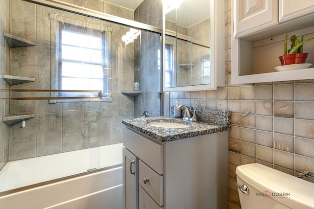 full bathroom featuring shower / bath combination with glass door, tile walls, vanity, decorative backsplash, and toilet