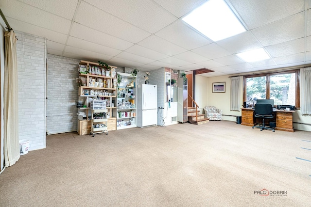 carpeted home office featuring a baseboard radiator, brick wall, and a paneled ceiling