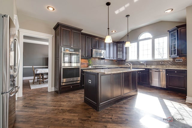 kitchen with dark brown cabinetry, a kitchen island, vaulted ceiling, appliances with stainless steel finishes, and tasteful backsplash