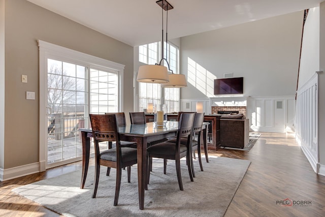 dining space featuring baseboards, wood finished floors, a high ceiling, a brick fireplace, and a decorative wall