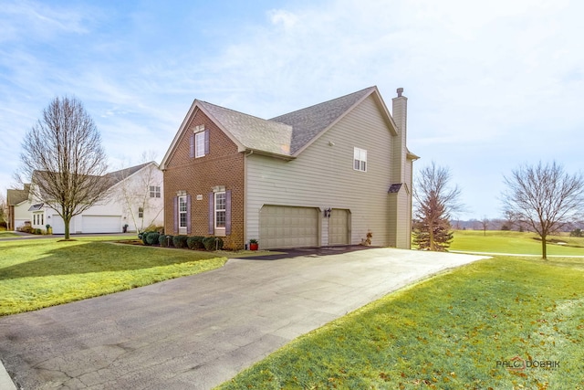 view of home's exterior featuring an attached garage, brick siding, driveway, a lawn, and a chimney