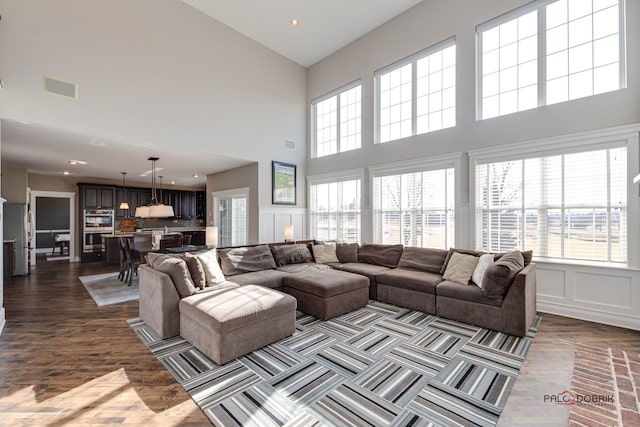 living room featuring dark wood-style flooring, visible vents, a decorative wall, and wainscoting