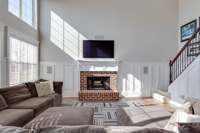 living room featuring a fireplace, a decorative wall, a towering ceiling, wood finished floors, and stairs