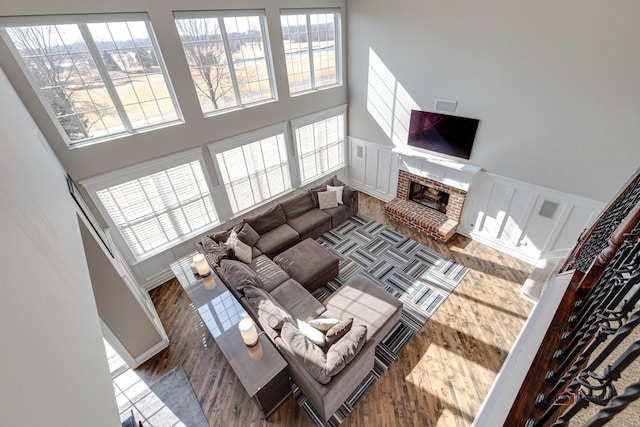 living room with a brick fireplace, a high ceiling, a decorative wall, and wood finished floors