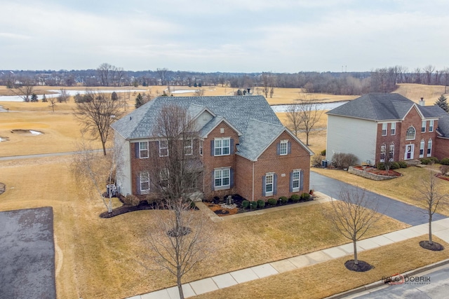 view of front of home featuring driveway, brick siding, roof with shingles, and a front lawn