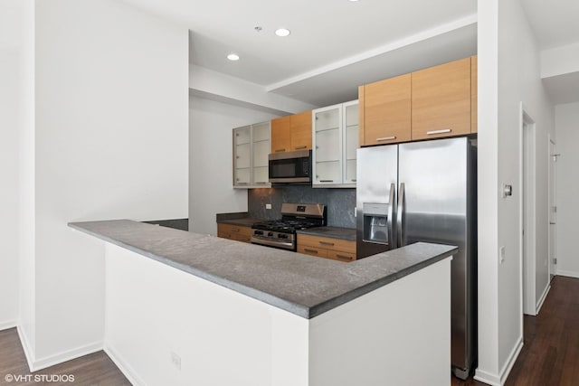 kitchen featuring tasteful backsplash, appliances with stainless steel finishes, glass insert cabinets, dark wood-style flooring, and a peninsula