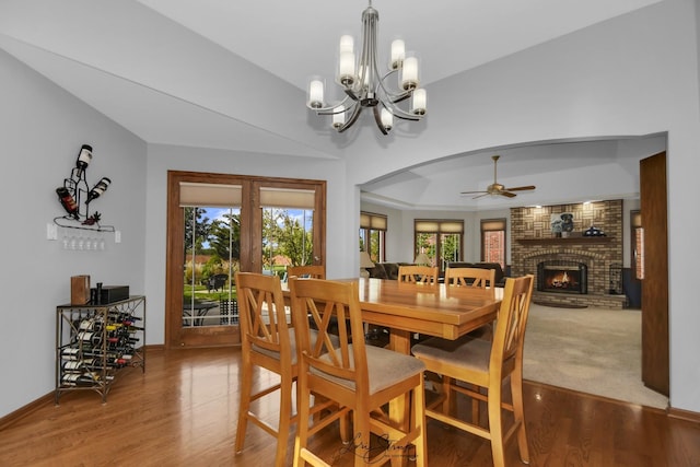 dining room with wood-type flooring, ceiling fan with notable chandelier, and a brick fireplace