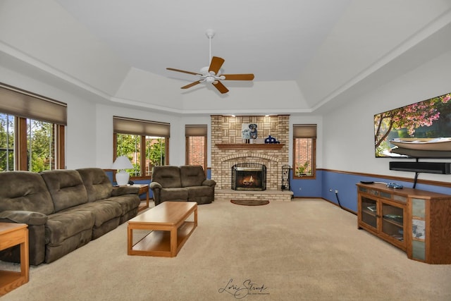 carpeted living room featuring a raised ceiling, a brick fireplace, and ceiling fan