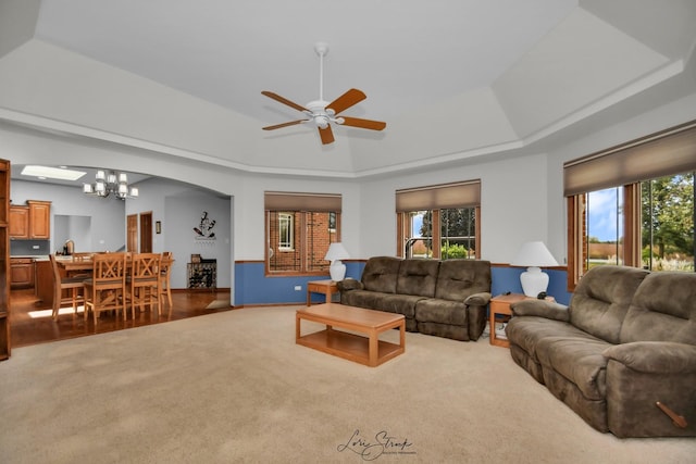 carpeted living room with a raised ceiling, ceiling fan with notable chandelier, and a wealth of natural light