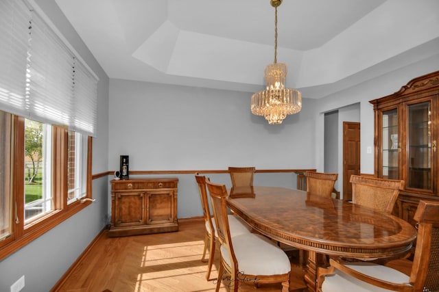 dining space with an inviting chandelier, light hardwood / wood-style floors, and a raised ceiling