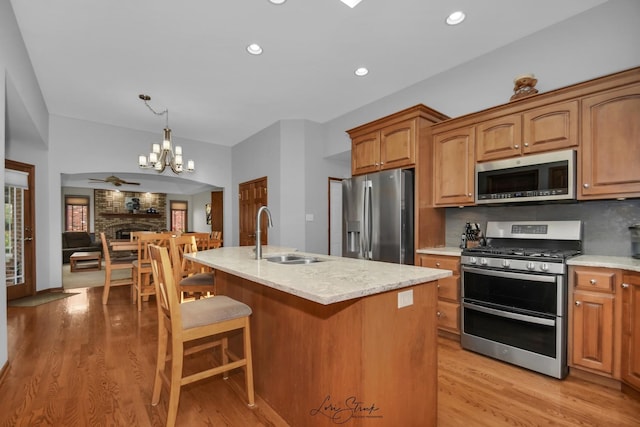 kitchen featuring decorative light fixtures, tasteful backsplash, sink, stainless steel appliances, and a center island with sink