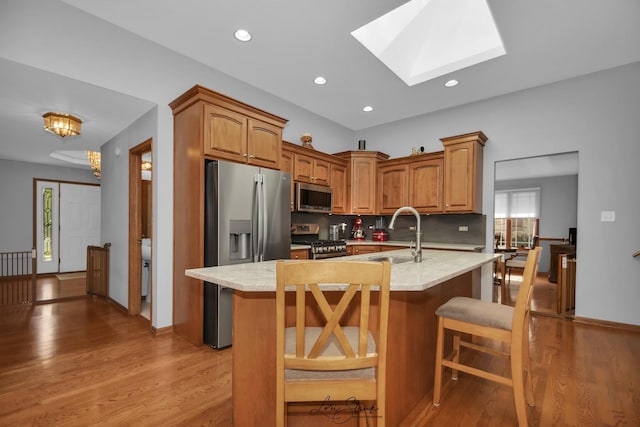 kitchen featuring sink, a breakfast bar area, backsplash, a skylight, and stainless steel appliances